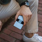 Man holding Steel Blue Evolve Smart Wallet beside leg, wearing cream joggers and sneakers