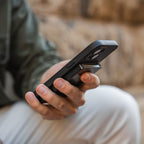 Close-up of Steel Blue Evolve Smart Wallet in hand while using phone outdoors
