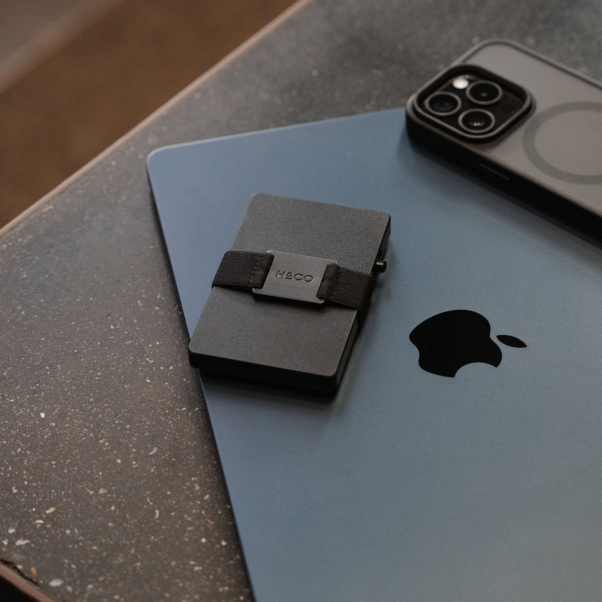 Midnight Black Evolve Smart Wallet resting on grey MacBook beside iPhone