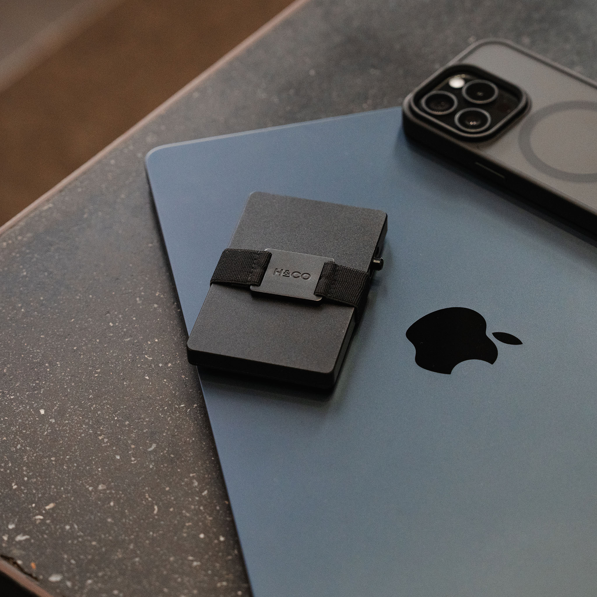 Midnight Black Evolve Smart Wallet resting on grey MacBook beside iPhone